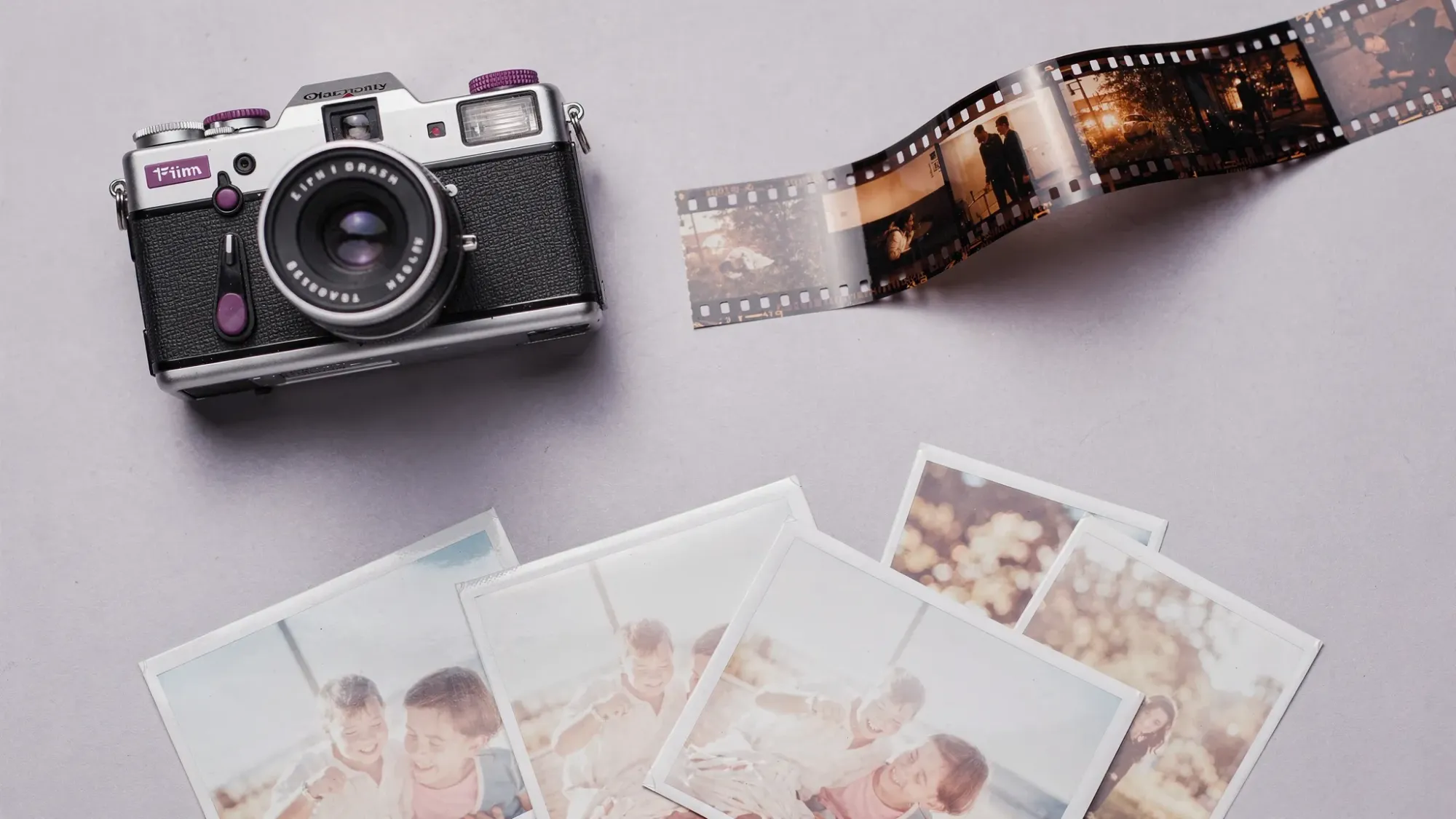 A flat lay of a disposable camera, a strip of 35mm negatives, and a few 4x6 photo prints on a tabletop, suggesting the steps of film development and scanning.