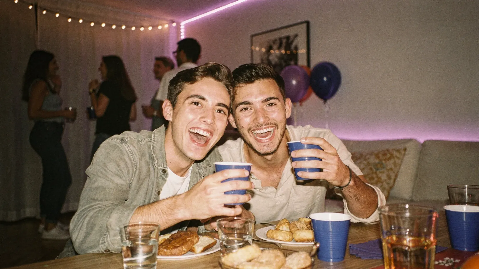 A candid indoor party scene shot from close range with direct flash, slightly warm tones, visible grain, and imperfect focus, resembling disposable camera photos while clearly taken on a modern smartphone.