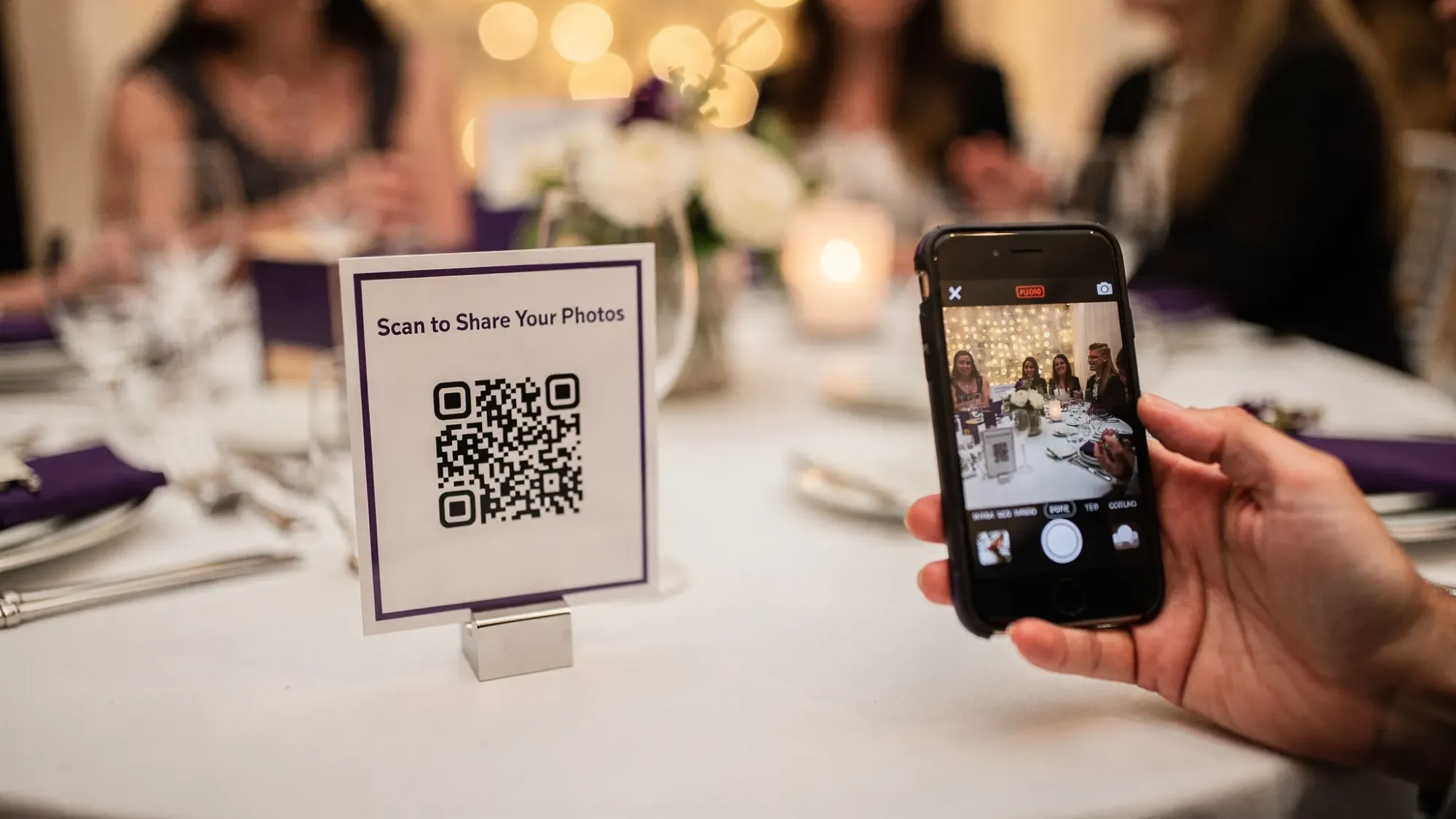 A simple event setup showing a printed QR code sign on a table next to a phone scanning it, representing instant guest photo sharing at a party or wedding.