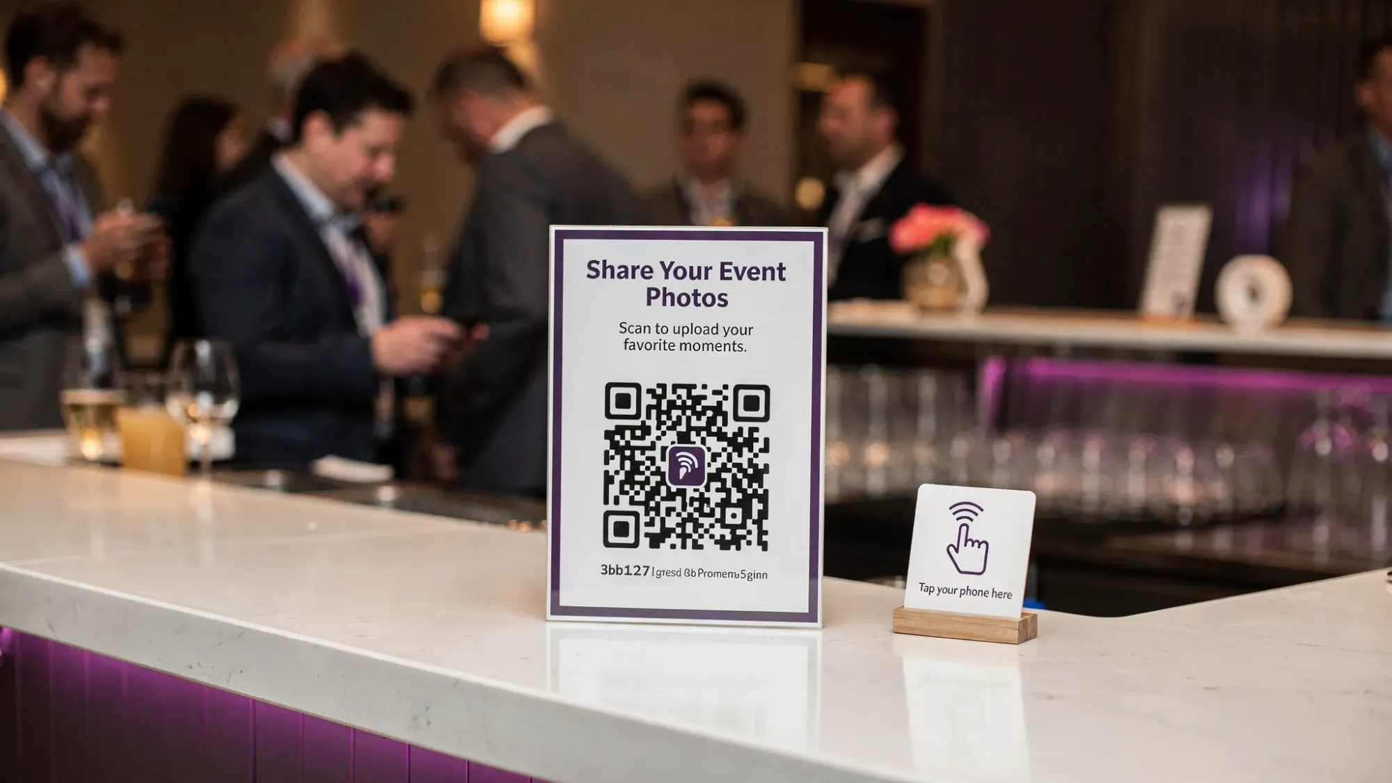 A real-world event setup showing a table tent with a QR code and a nearby NFC tag sign, placed at a reception bar area so guests naturally scan and contribute photos.