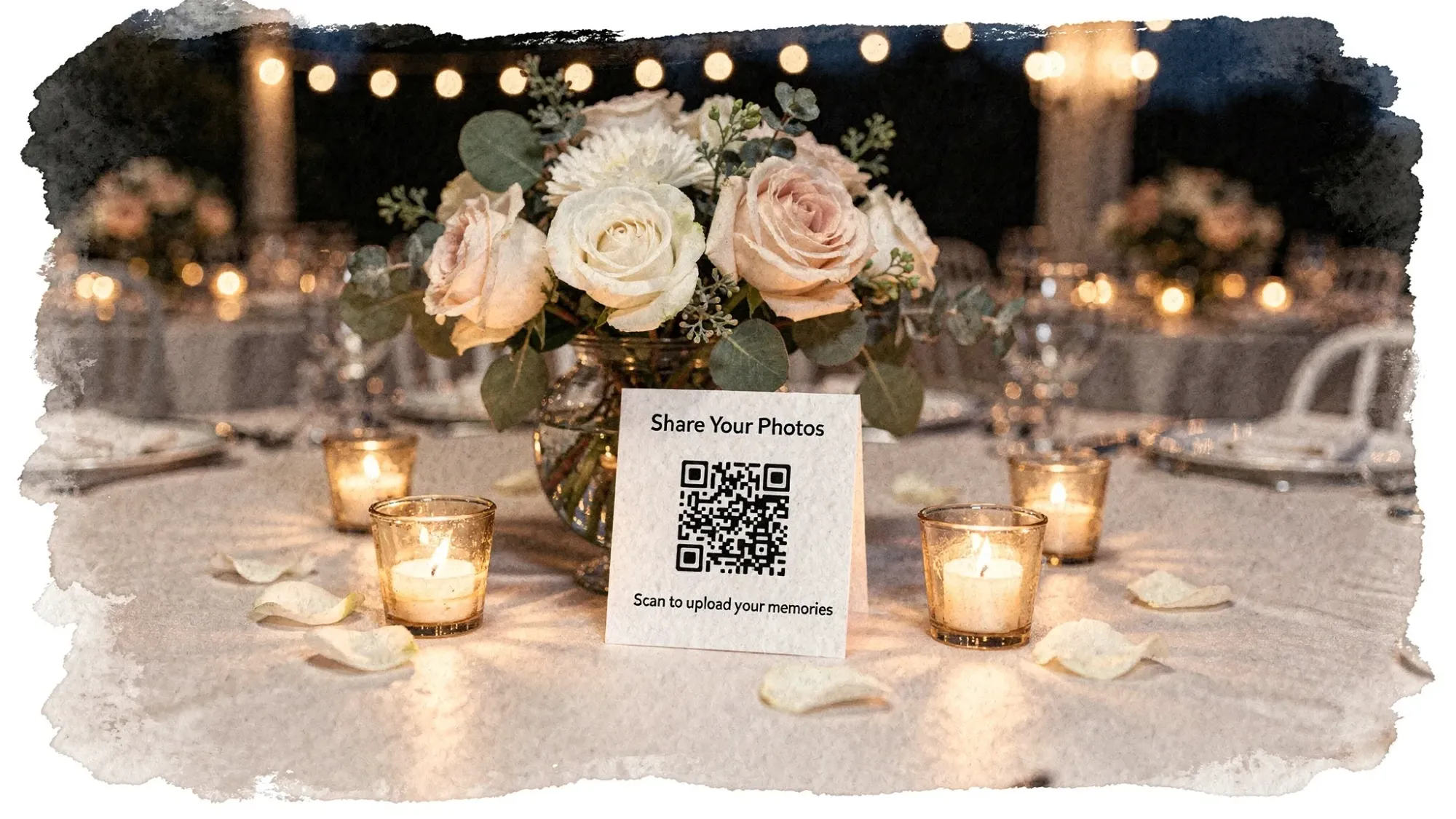 A wedding reception table setup featuring a small tent card with a QR code that invites guests to share photos, placed next to a centerpiece and candles in warm ambient light.